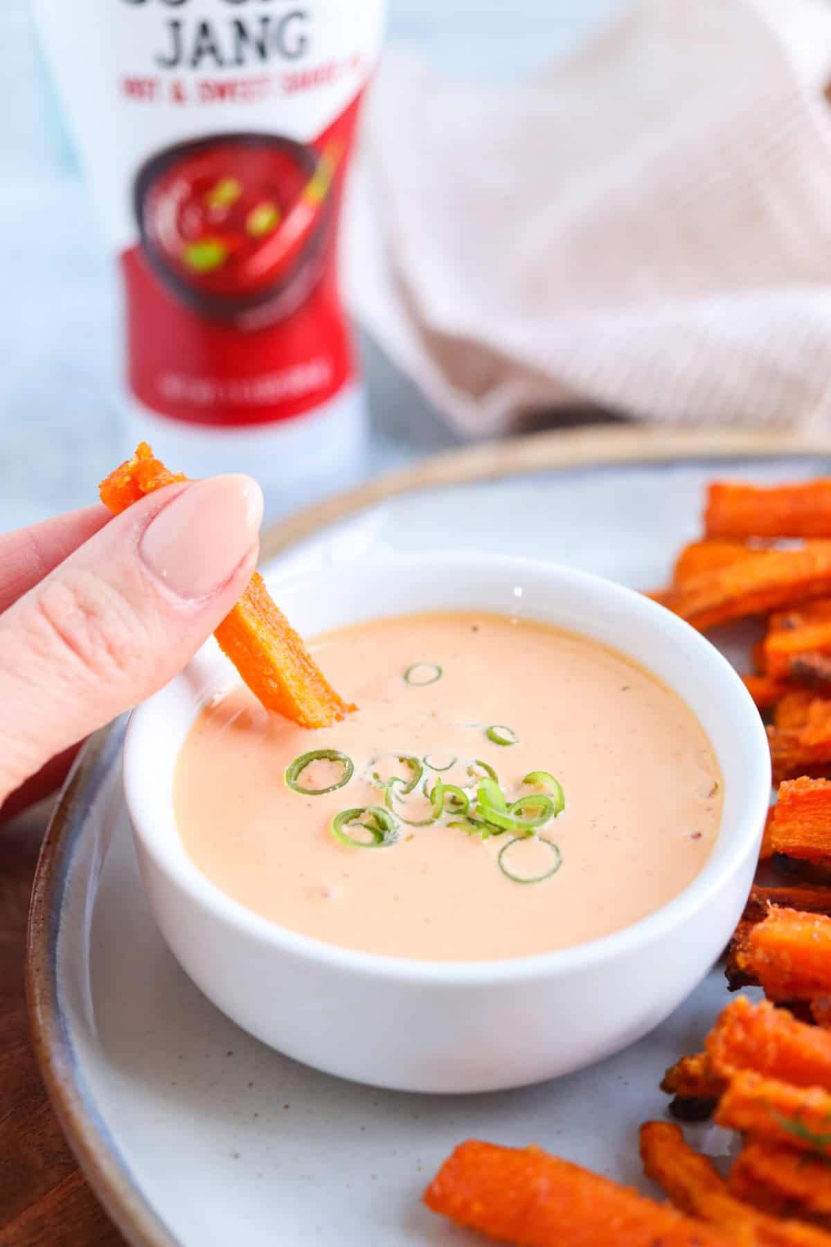 Gochujang aioli in a small white bowl surrounded by carrot fries, one fry being dipped.