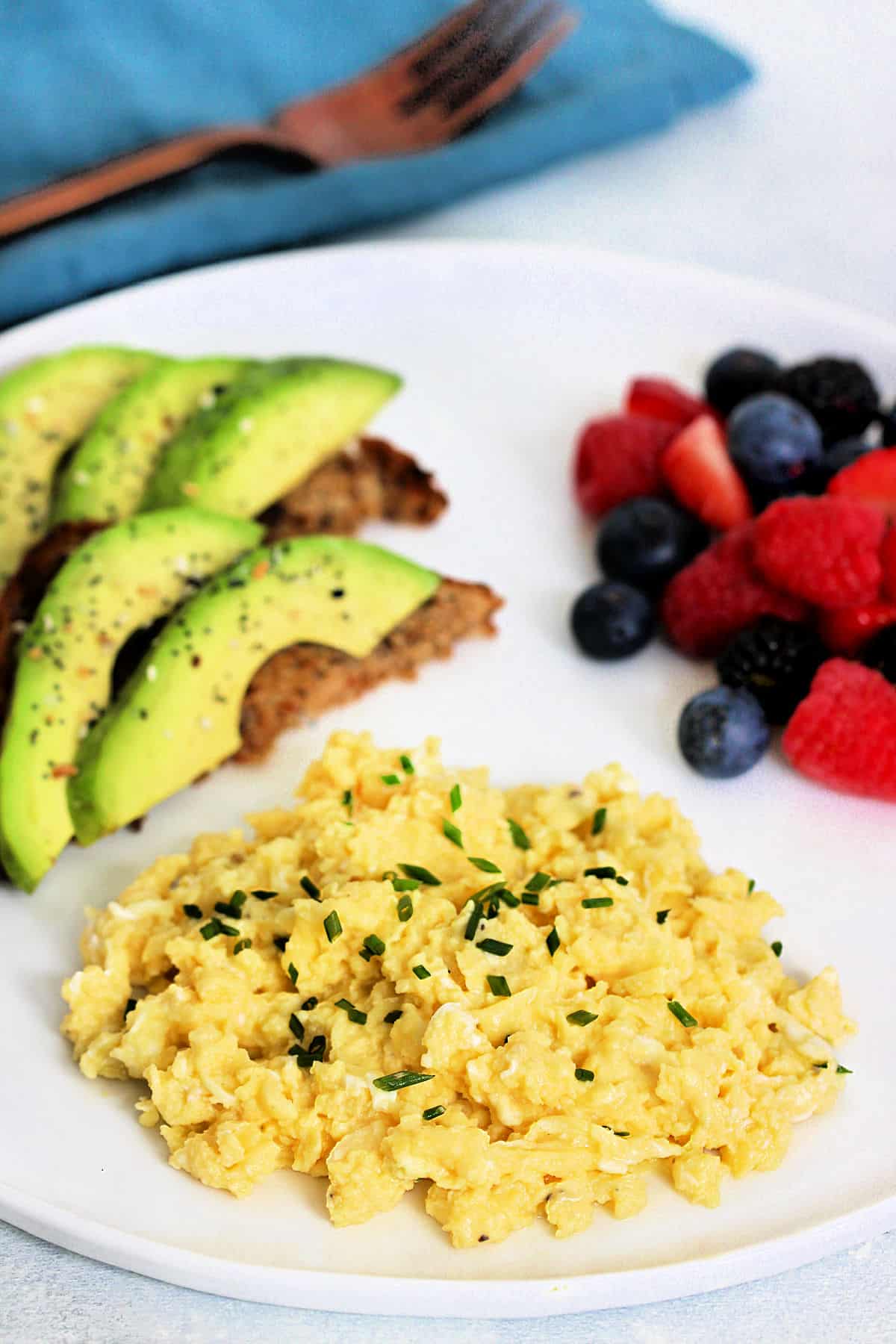 cottage cheese scrambled eggs on a white plate with avocado toast and berries.