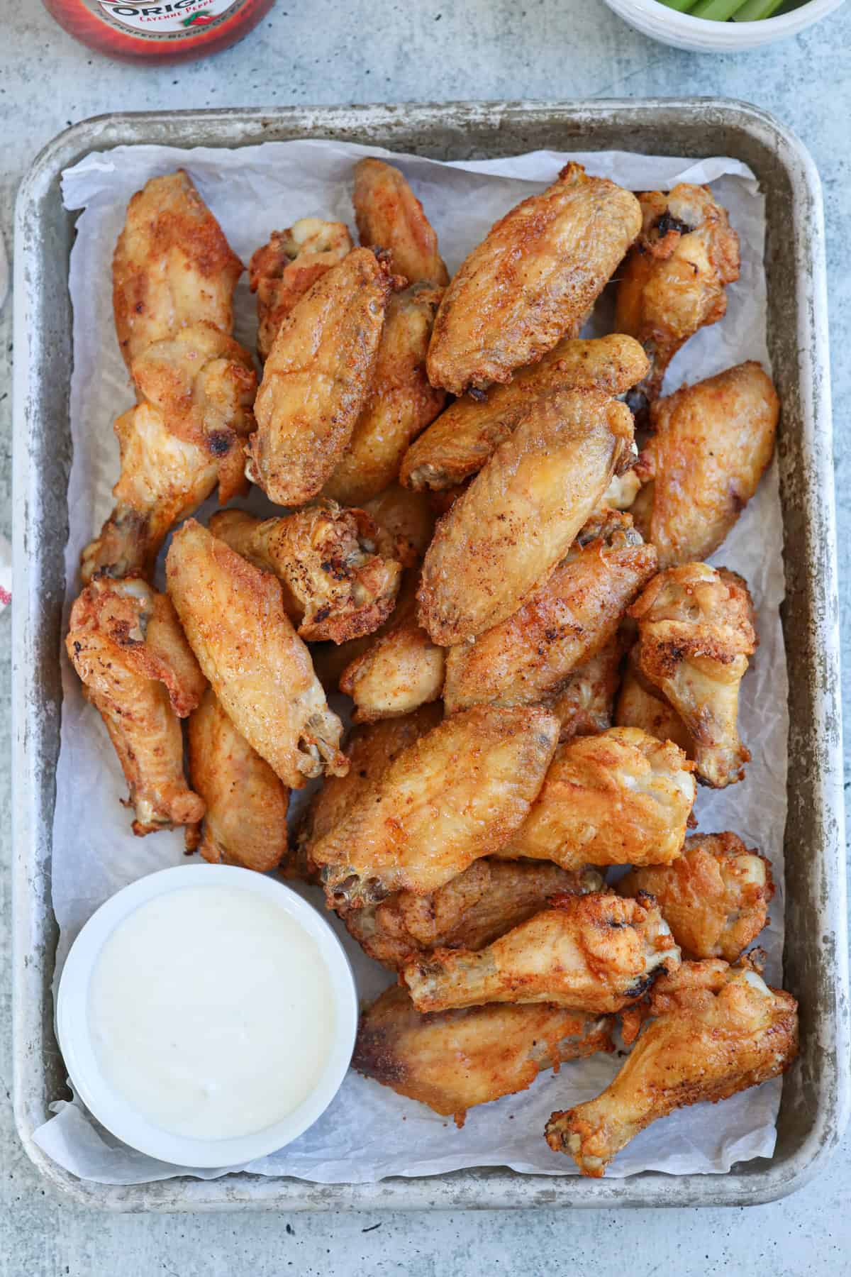 baked chicken wings on a pan with a side of white sauce in a small ramekin.