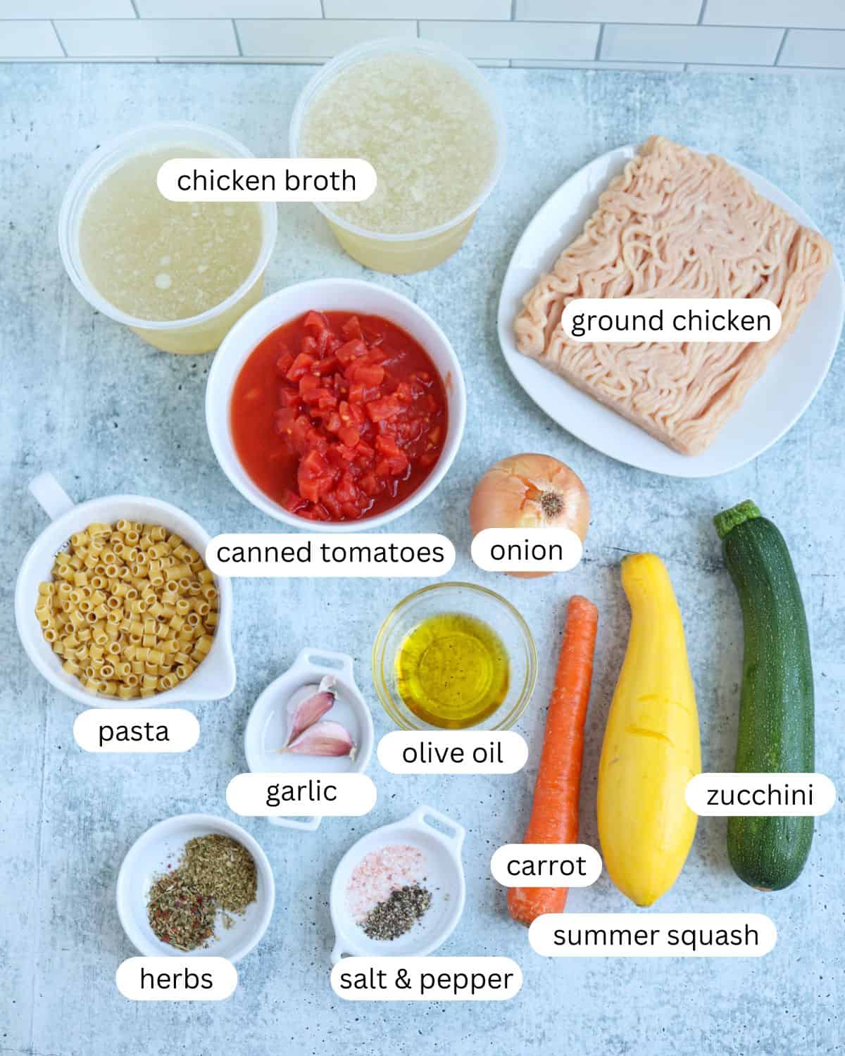 ingredients for making ground chicken soup with veggies on a gray counter with captions.