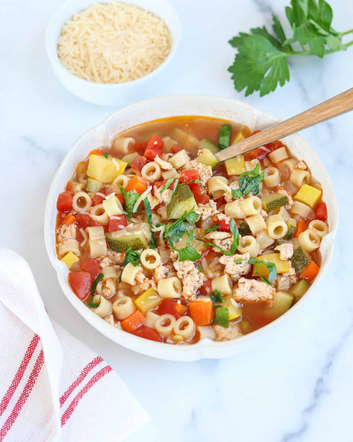 a bowl of ground chicken soup with zucchini, summer squash, tomatoes and small pasta.