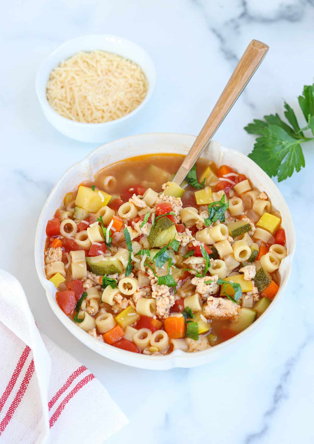 a bowl of ground chicken soup with zucchini, summer squash, tomatoes and small pasta.