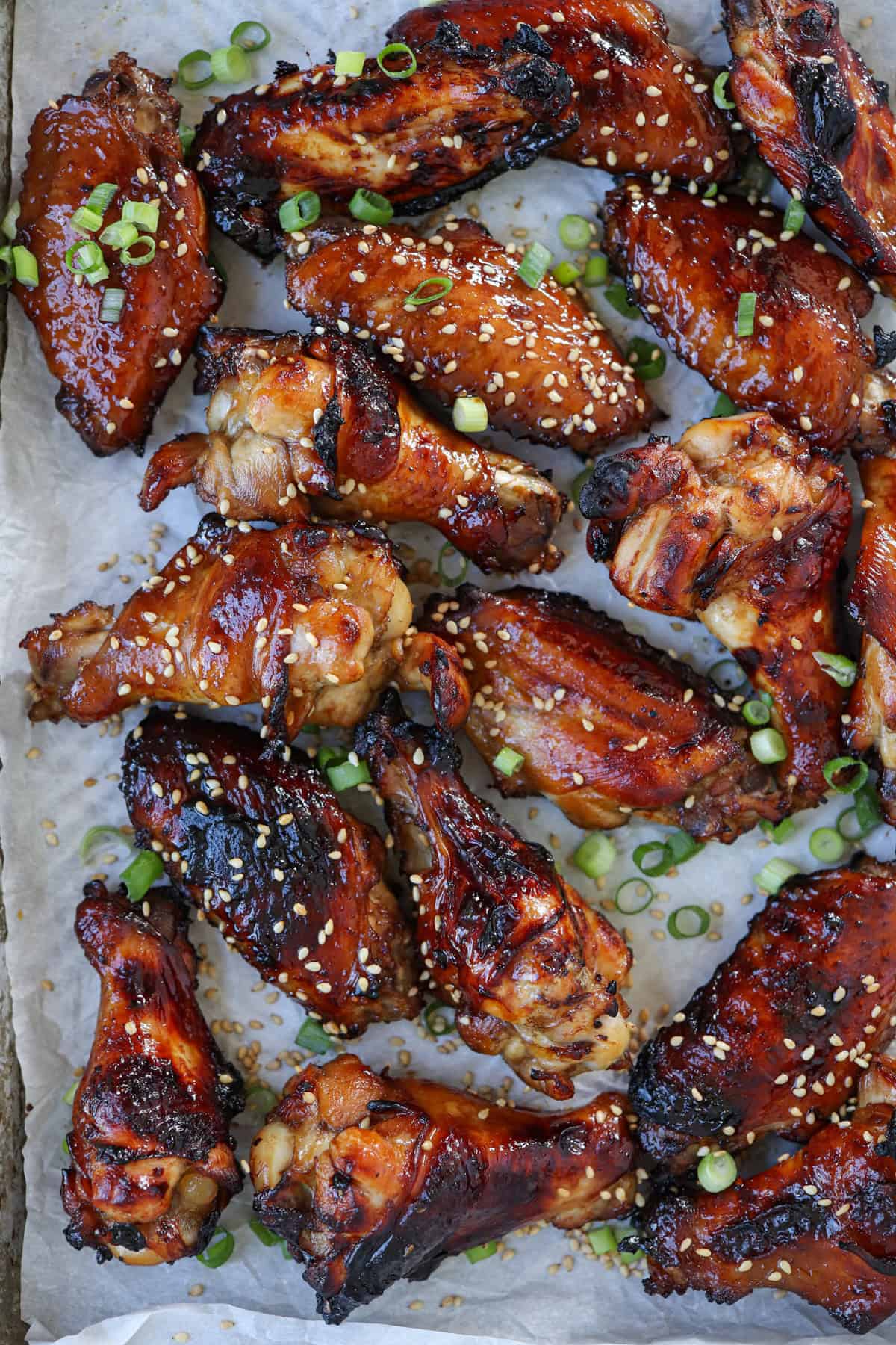 sticky soy garlic baked chicken wings on paper garnished with green onions and sesame seeds.