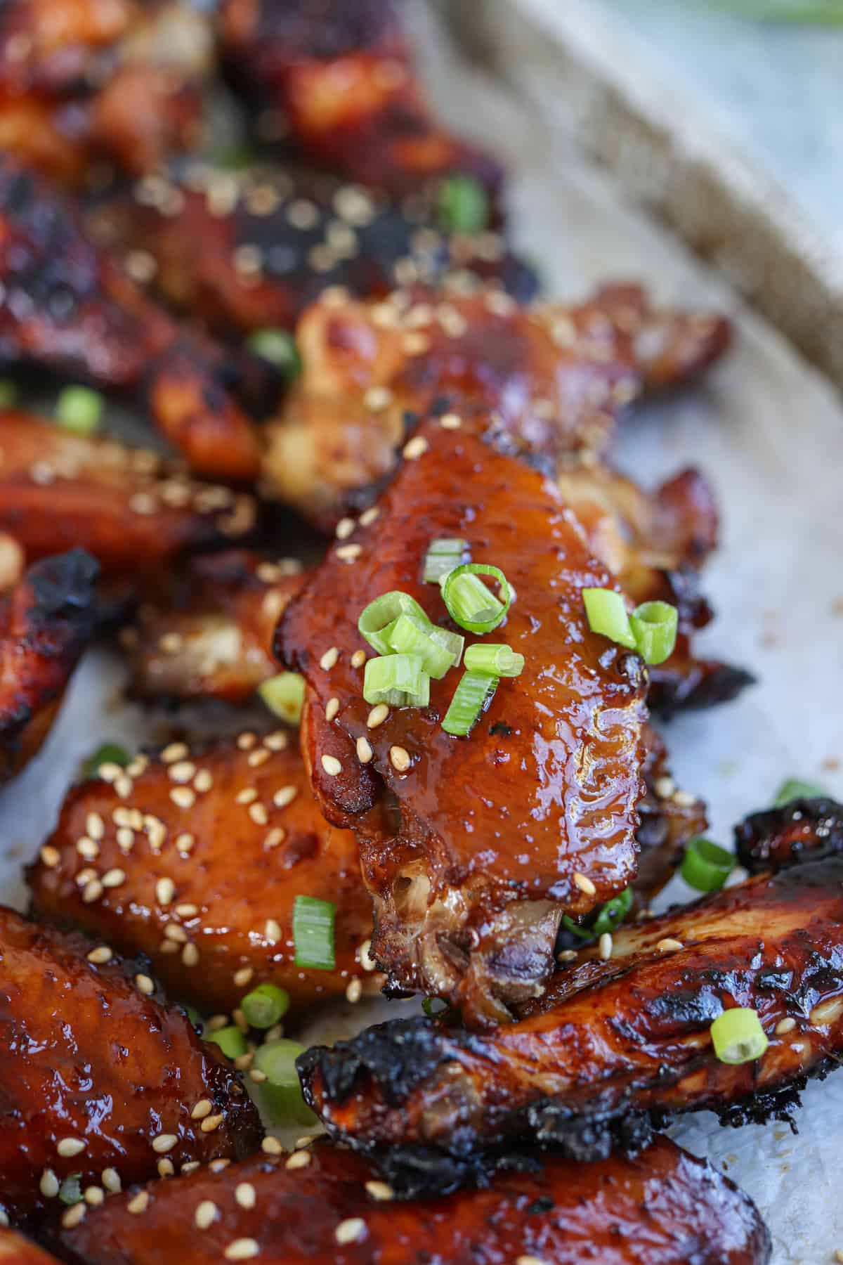 sticky soy garlic baked chicken wings on paper garnished with green onions and sesame seeds.