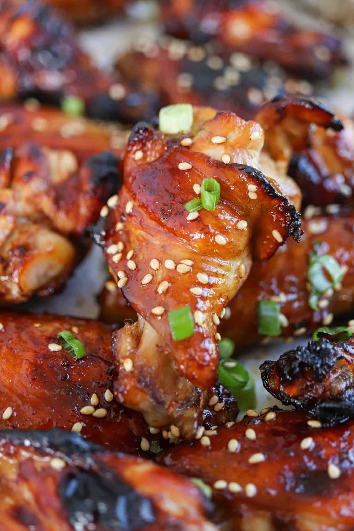 sticky soy garlic baked chicken wings on paper garnished with green onions and sesame seeds.