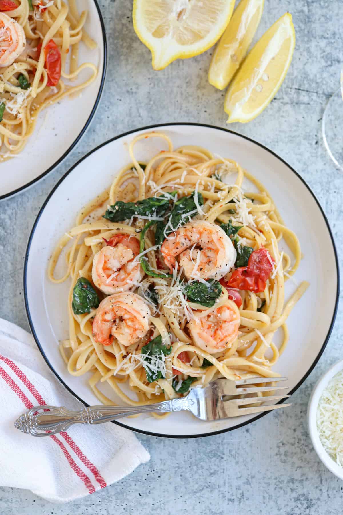 pasta with shrimp, cherry tomatoes and spinach on a plate on gray surface.