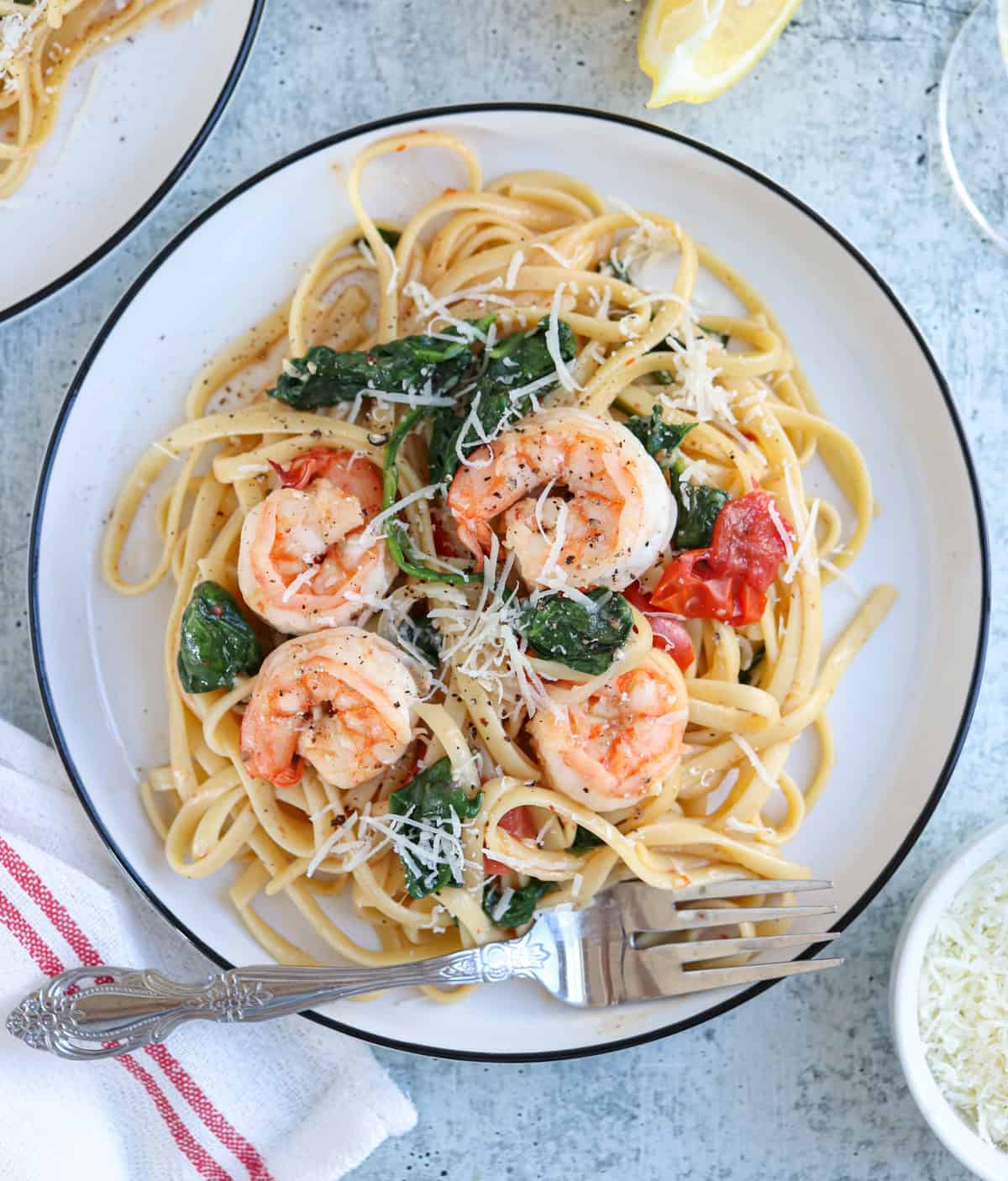 pasta with shrimp, cherry tomatoes and spinach on a plate on gray surface.