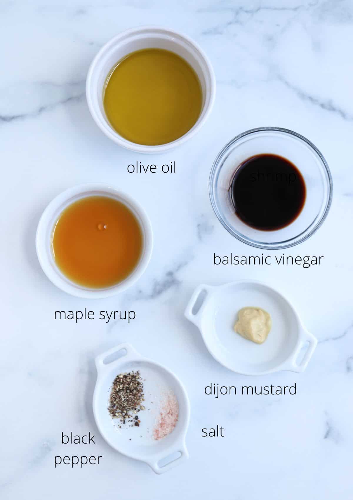 Ingredients arranged on a marble surface for a falafel platter: olive oil, balsamic vinegar, maple syrup, Dijon mustard, black pepper, and salt. Each ingredient is in a small white dish, labeled with its name.