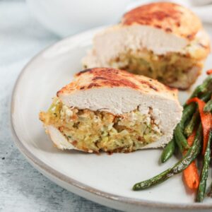 A plate with two pieces of stuffed chicken breast, showcasing a golden crispy exterior and a savory filling. Served alongside sautéed green beans and thinly sliced carrots.