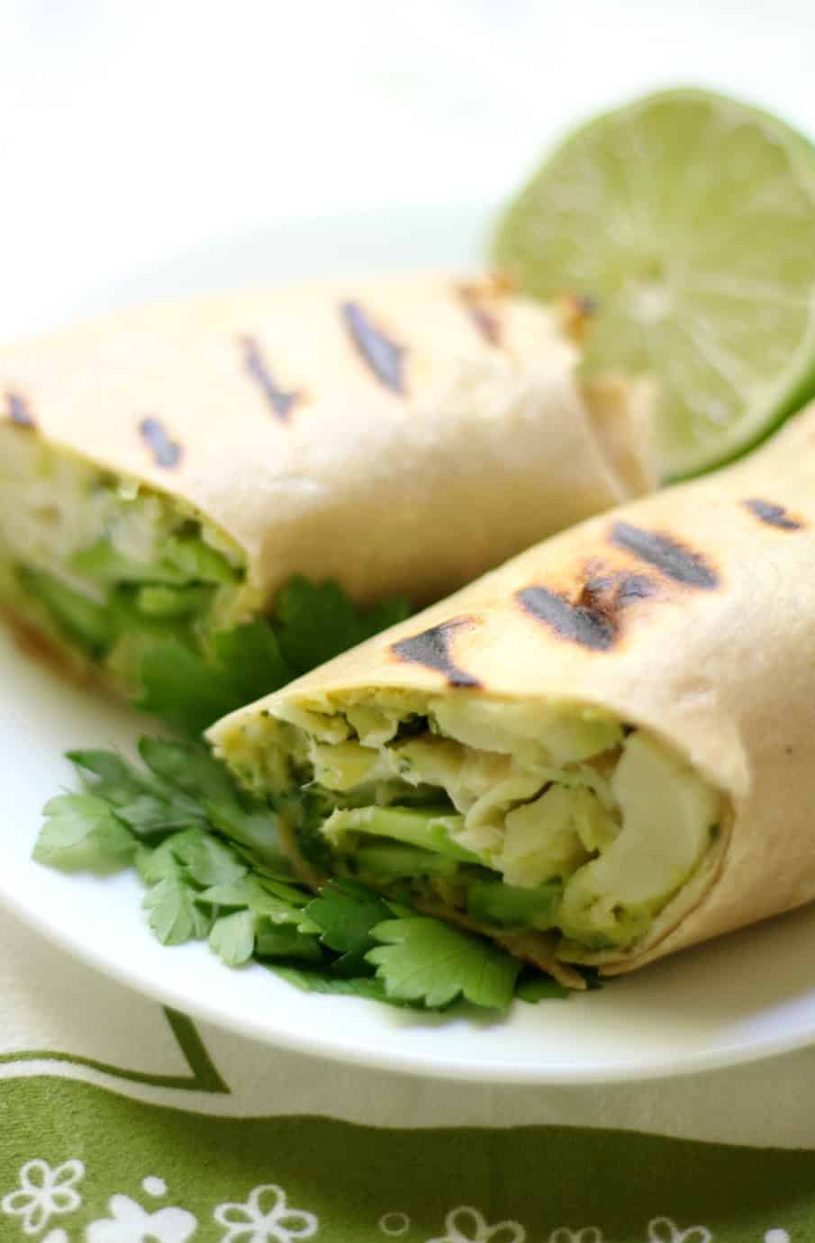 Two grilled wraps filled with lettuce and vegetables are cut in half and placed on a white plate. A slice of lime and fresh parsley garnish the plate.