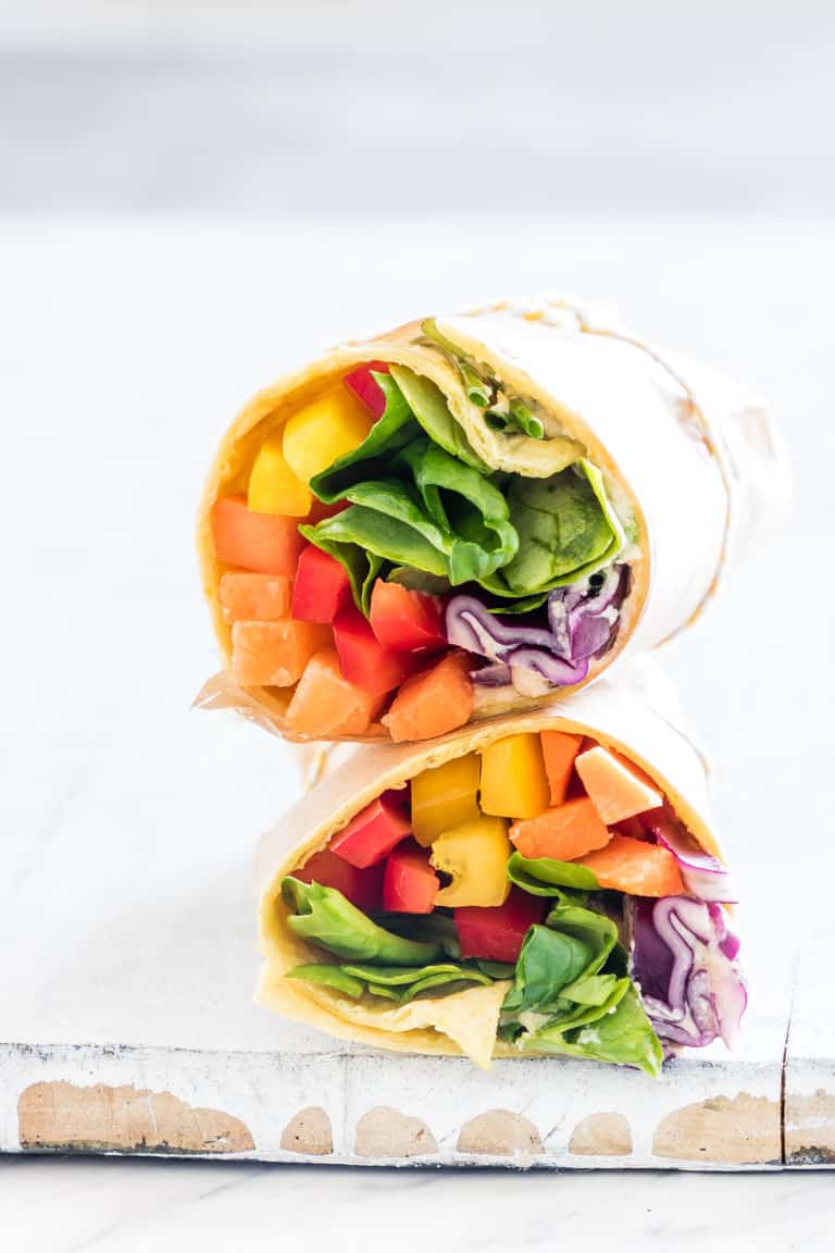 Two colorful veggie wraps halved, showcasing layers of spinach, shredded purple cabbage, sliced bell peppers, and carrots, neatly stacked on a light wooden surface.