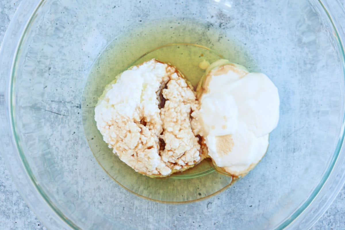 A glass mixing bowl containing four egg whites, creamy cottage cheese, and vanilla extract on a gray surface.