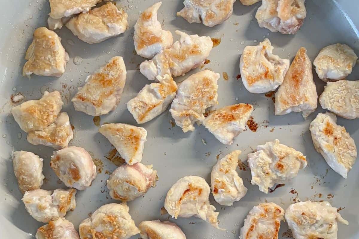 Chunks of cooked chicken breast, lightly browned, scattered in a frying pan.