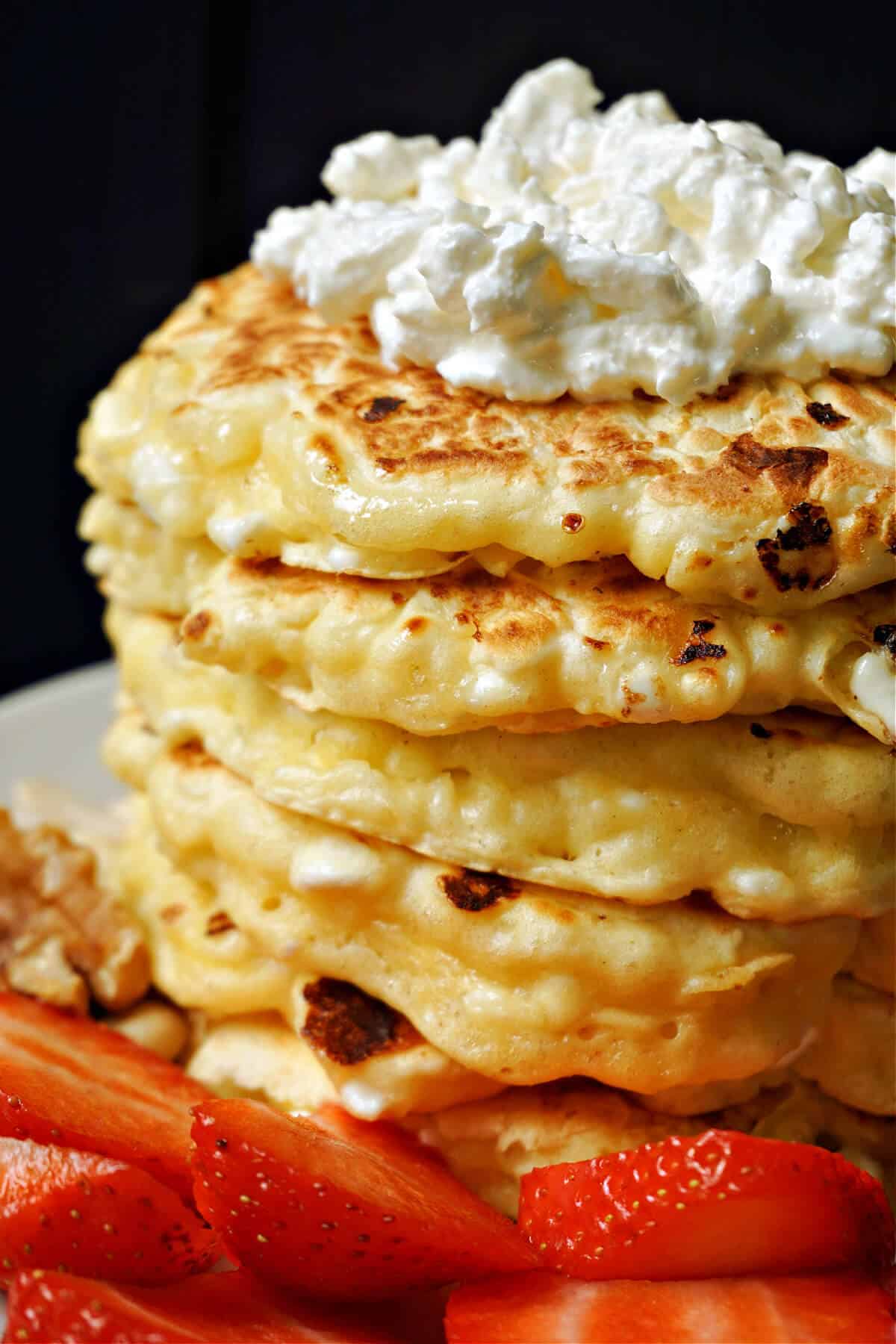 A stack of fluffy, golden pancakes topped with whipped cream. The pancakes are slightly charred. Sliced fresh strawberries are placed at the base, adding a pop of color.
