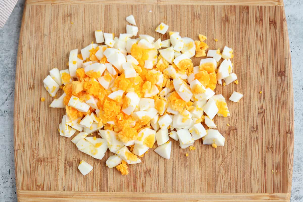 Chopped hard-boiled eggs, with white and yellow yolk pieces, are scattered on a wooden cutting board.