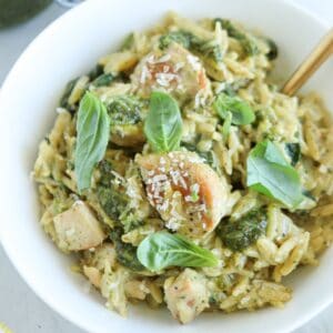 A bowl of orzo pasta with tender pesto chicken pieces, topped with fresh basil leaves and a sprinkle of grated Parmesan cheese.
